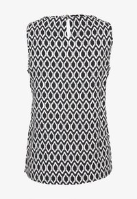 Haut sans manches avec un motif géométrique noir et blanc, col rond, et une petite fermeture par bouton au dos. Texture de tissu lisse.