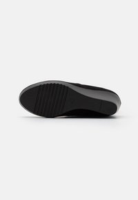 Semelle de chaussure noire avec une surface en caoutchouc texturée, présentant des rainures horizontales et un bord incurvé. Le matériau semble durable et flexible.
