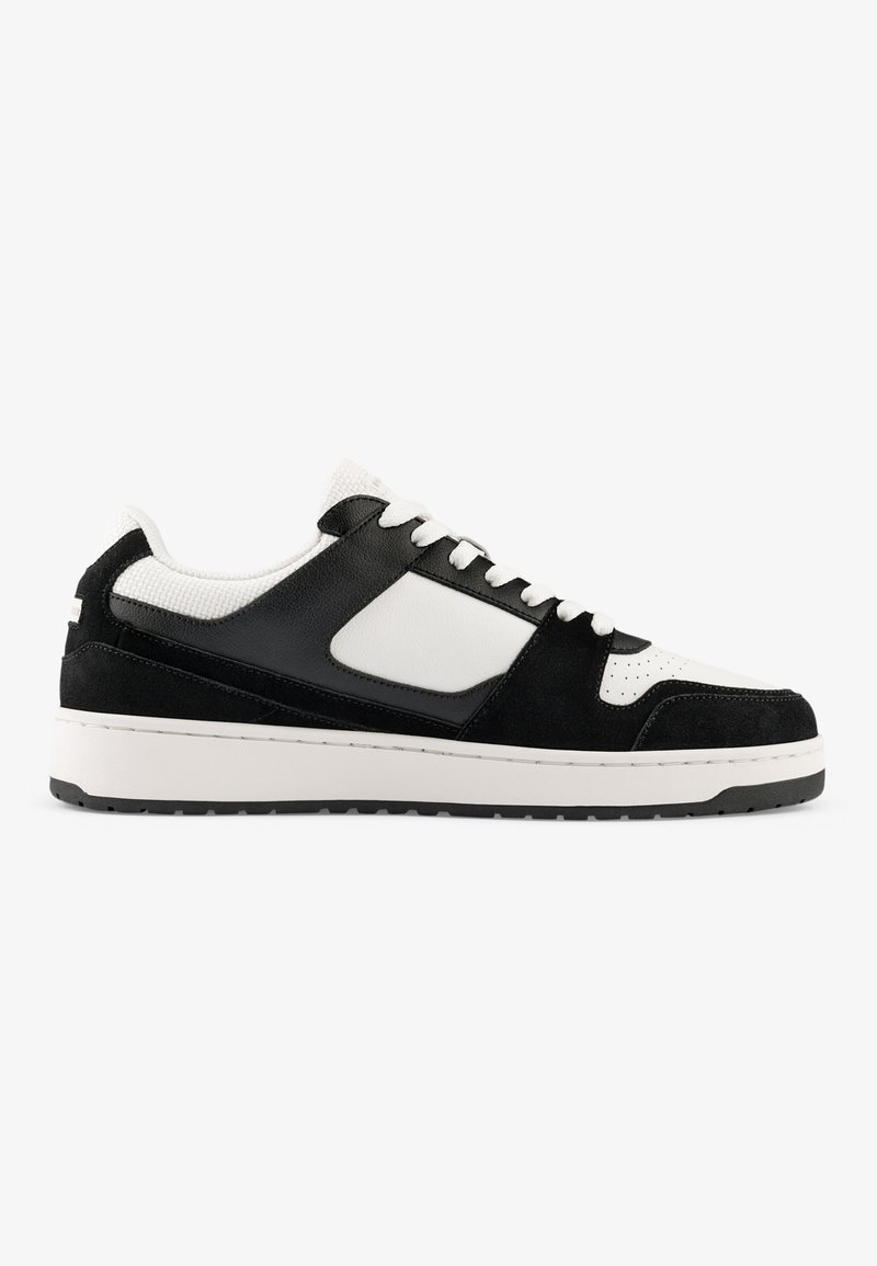 Black and white sneakers with suede and mesh materials, round toe, padded collar, and a textured outsole. Features white laces and accents.