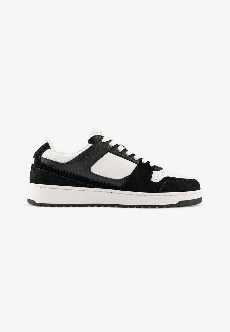 Black and white sneakers with suede and mesh materials, round toe, padded collar, and a textured outsole. Features white laces and accents.