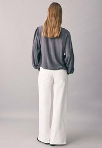 Blouse grise à manches longues avec épaules plissées, associée à un pantalon large blanc. Tissu lisse avec une coupe décontractée et des détails de couture minimalistes.