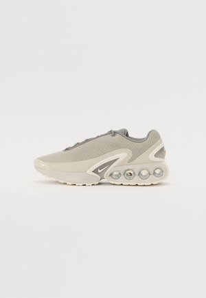 Chaussure de sport gris clair avec empeigne en mesh, semelle intermédiaire rembourrée comportant quatre unités d’air circulaires visibles, et petit logo Swoosh près de la semelle.
