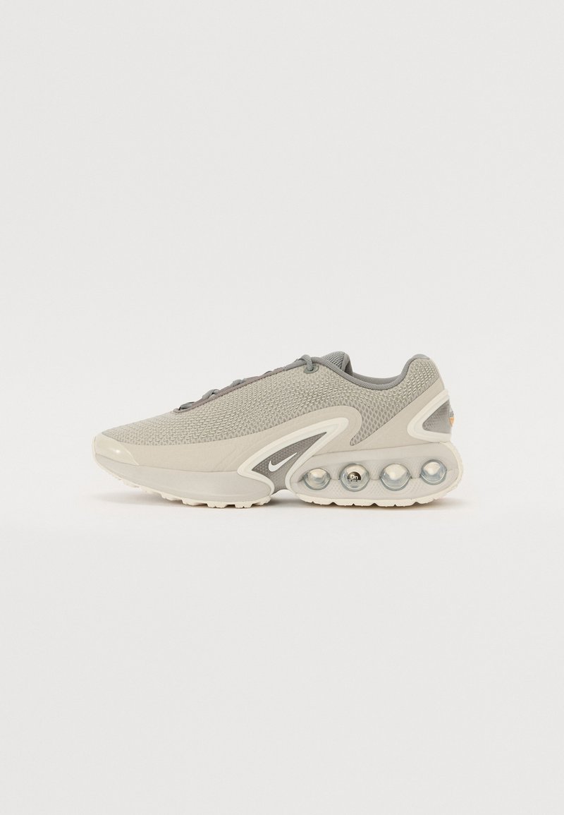 Chaussure de sport gris clair avec empeigne en mesh, semelle intermédiaire rembourrée comportant quatre unités d’air circulaires visibles, et petit logo Swoosh près de la semelle.