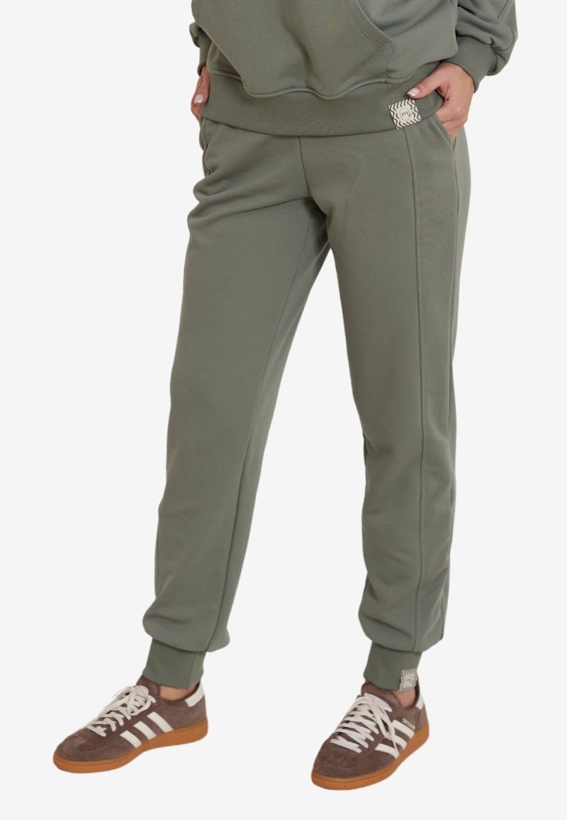 Oliwkowe dresy z elastycznymi mankietami, bocznymi kieszeniami i naszywką z logo. Wykonane z miękkiego, teksturowanego materiału zapewniającego komfort.