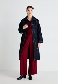 Denim coat with contrasting white stitching, layered over a burgundy knit top and wide-legged burgundy pants, paired with black ankle boots.