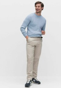Lichtblauwe kabelgebreide trui, beige broek en marineblauwe sneakers. De outfit heeft een casual pasvorm en textuurstof met geribde manchetten.
