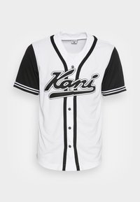 Bílý baseballový dres s černými krátkými rukávy, kontrastními předními knoflíky a černým kurzívním logem "Kani" přes hrudník.
