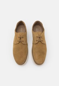 Paire de chaussures décontractées en daim beige avec deux œillets et semelles beiges vues de dessus sur fond blanc.