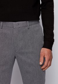 Szare, dopasowane spodnie wykonane z tkaniny o fakturze z delikatnym wzorem, uzupełnione standardowym paskiem i bocznymi kieszeniami.