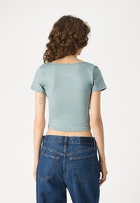 Rövid ujjú, cropped top puha, világoskék anyagból, magas derekú, sötét mosású farmerral párosítva, amely klasszikus hátsó zsebekkel és varrással rendelkezik.