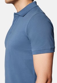 Koszulka polo z krótkim rękawem w jednolitym niebieskim kolorze, z kołnierzykiem i teksturowanym materiałem, z widocznymi szwami na rękawach i końcówkach.