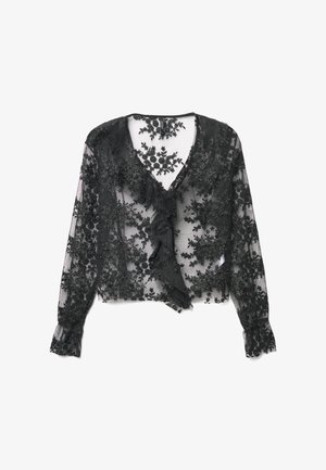 Blouse en dentelle noire avec col en V, manches longues, broderie florale, détail à volants sur le devant et texture transparente. Les manches se terminent par des poignets élastiques.