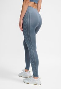 Graue hoch-taillierte Leggings mit strukturierten Zickzackmustern an den Seiten. Aus dehnbarem Stoff gefertigt, kombiniert mit weißen Sportschuhen.