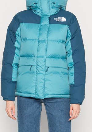 Portant une doudoune North Face bleu sarcelle et bleu marine avec poches zippées et col montant, associée à un jean bleu.
