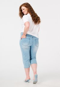 Un pantalon capri en denim bleu clair avec une coupe décontractée, doté de deux poches au dos et d'un ourlet roulé. Associé à une chemise blanche à manches courtes.