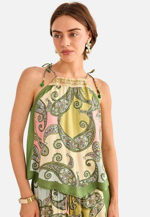 Mujer con un top halter sin mangas de patrón de cachemira en tonos verdes, rosas y beige, combinado con pantalones a juego y pendientes florales.