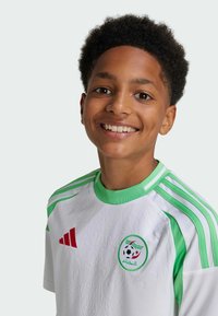 Witte voetbalshirt met groene accenten en Adidas-stripes, met een gemêleerd ontwerp en een cirkelvormig Algerijns embleem op de borst.