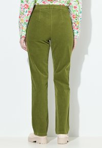 Grüne Cordhosen mit geradem Bein, hinteren Taschen und hohem Bund, kombiniert mit hellgefärbten Schuhen.