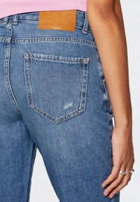 Světle modré džínové kalhoty s hnědou koženou etiketou označenou "ONLY BLUE DENIM." Mají klasický design s pěti kapsami a odřené detaily.