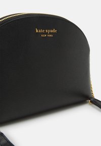 Svart strukturerad handväska med en texturerad yta, gulddragkedja och logotyp präglad på framsidan. Har en kedjad detalj på remmen.