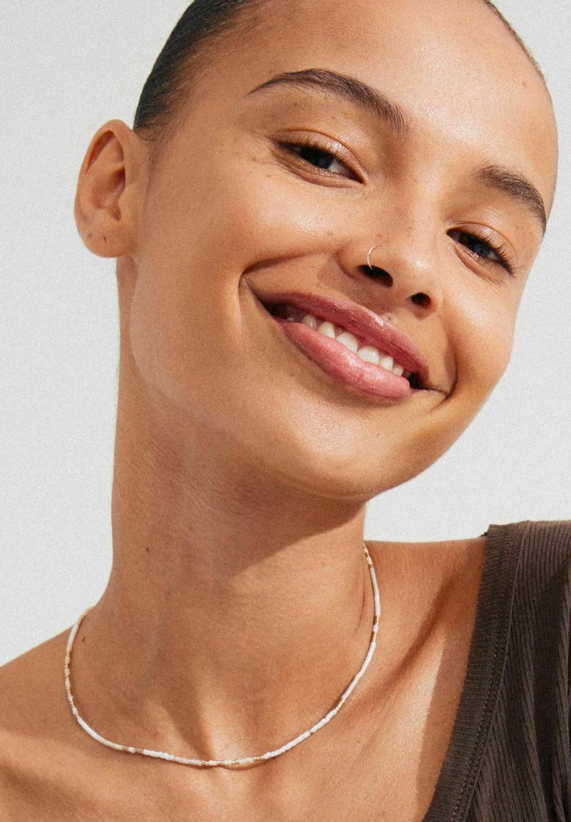 Beaded necklace with alternating white and gold accents, slender design, worn around a neck with a smooth, natural skin texture.
