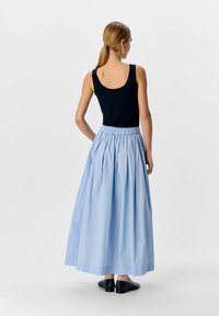 Lys blå, gulvlang nederdel med samlet talje og sidelommer, parret med en tætsiddende sort tanktop og sorte flade sko.