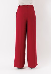 Pantaloni larghi rossi con tessuto morbido, vita regolata, tasche laterali e vestibilità ampia. Presentano un design pulito e minimalista.