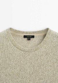 Beige neulepaita pyöreällä kaula-aukkolla, jossa on kuvioitu pintakuvio ja pieni sisäinen merkintä, jossa on brändin tiedot.