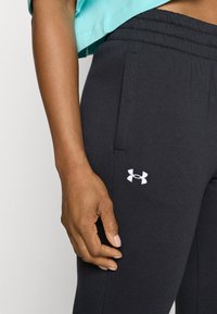 Svarta mjukisbyxor med dragsko i midjan, utrustade med sidofickor och en vit Under Armour-logotyp på vänster lår. Mjukt, stretchigt tyg.