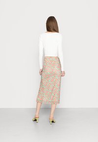 Saia longa floral em azul claro com flores vermelhas e verdes, combinada com um top cropped branco e mules de salto verdes. Tecido suave e leve.