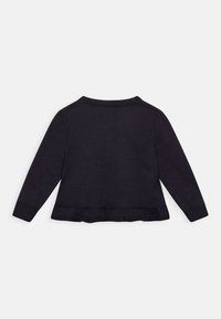 Mörk marinblå stickad tröja med långa ärmar, ribbad manschett och volangkant. Har en enkel rund halsringning och en mjuk yta.