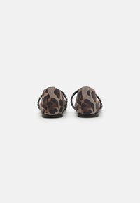 Bailarinas de ante con estampado de leopardo, con un tacón bajo, lados abiertos y acentos trenzados en la parte posterior. Esquema de colores en marrón y negro.