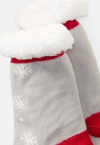 Pilki megzti kojinės su baltomis snaigėmis ir raudonais akcentais. Viršus apklotas minkštu, pūkuotu baltu medžiagos sluoksniu.