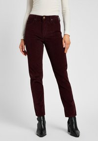 Burgundy corduroy jeans with a fitted design, featuring front pockets, a top button closure, and a soft texture. Paired with black ankle boots.