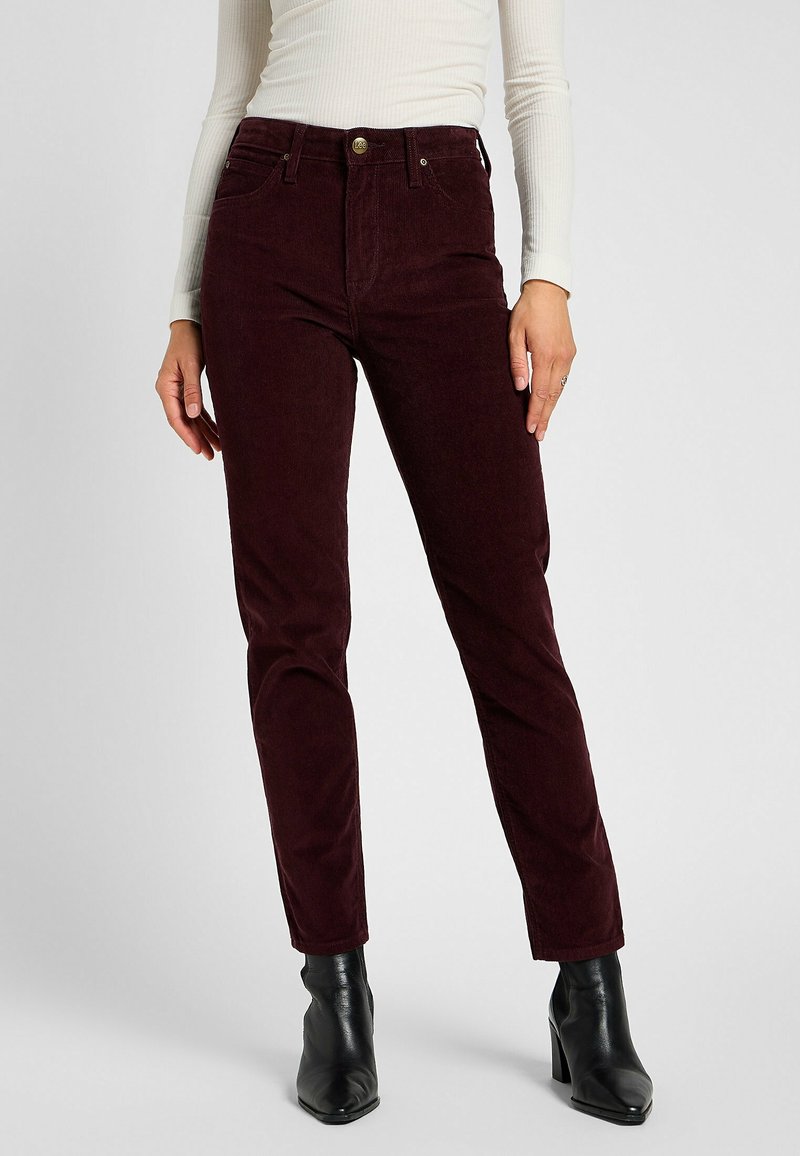 Burgundy corduroy jeans with a fitted design, featuring front pockets, a top button closure, and a soft texture. Paired with black ankle boots.