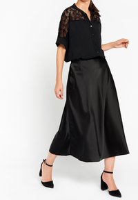 Blusa nera con dettagli in pizzo sulle spalle, abbinata a una lunga gonna nera in satin fluida. Tacchi a strappo neri completano l'outfit.