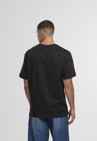 Fekete pamut póló kerek nyakkivágással és rövid ujjakkal, laza szabással és egyenes aljú kialakítással, hátulról bemutatva.