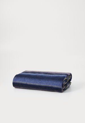 Couverture en laine tissée de couleur bleu foncé avec des rayures bleu clair et violettes. Pliée, mettant en valeur une texture lisse et des bords nets.
