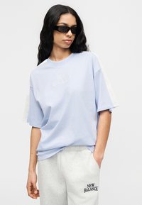 Ανοιχτό μπλε βαμβακερό μπλουζάκι με κοντά μανίκια, με λευκές λεπτομέρειες και το λογότυπο "NEW BALANCE" κεντημένο στο στήθος. Κανονική εφαρμογή.