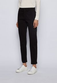 Pantalones de mezcla de algodón negros con un ajuste slim, bolsillos frontales, trabillas para cinturón y una textura suave, combinados con zapatillas blancas.