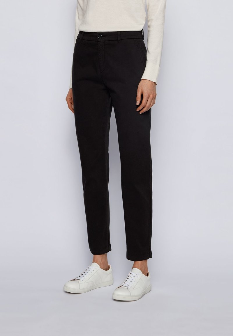 Pantalones de mezcla de algodón negros con un ajuste slim, bolsillos frontales, trabillas para cinturón y una textura suave, combinados con zapatillas blancas.