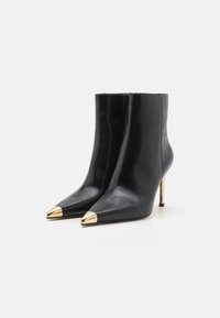 Mustad musta nahast ankle boots, millel on teravad varbad ja metalne kuldne kate varba kohal. Kõrgendatud stilettokand käib. Sile tekstuur, voolujooneline disain.