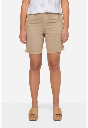 Shorts beiges en tissu lisse, dotés de poches avant et de coutures surpiquées. Associés à des sandales à plateforme beige.