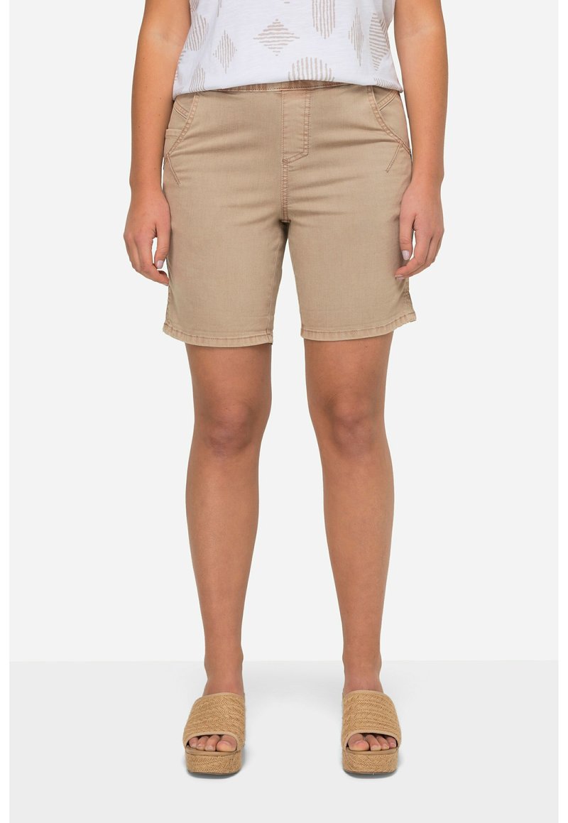 Pantaloni corti beige in tessuto liscio, con tasche frontali e cuciture a vista. Abbinati a sandali con plateau color sabbia.