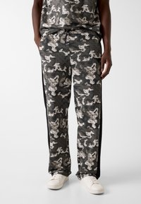 Joggingbroeken met camouflagepatroon in donker groen en beige, gemaakt van zachte stof met een elastische tailleband en zijzakken, met contrasterende zwarte strepen.