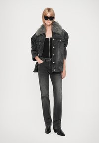 Μαύρο τζάκετ από τζην με τεχνητό κολάρο από γούνα, σε συνδυασμό με μαύρο τοπ χωρίς μανίκια και σκούρους γκρι παντελόνες σε ίσια γραμμή. Λαμπερές μαύρες ψηλές μπότες.