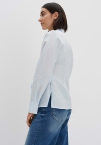 Camicia a maniche lunghe a righe blu chiaro con colletto, polsini abbottonati e spacchi laterali, abbinata a jeans in denim. Texture liscia.