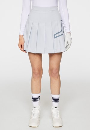Gonna plissettata azzurro chiaro con vita solida e un accento di design geometrico. Indossata con sneakers bianche e calze a righe navy.