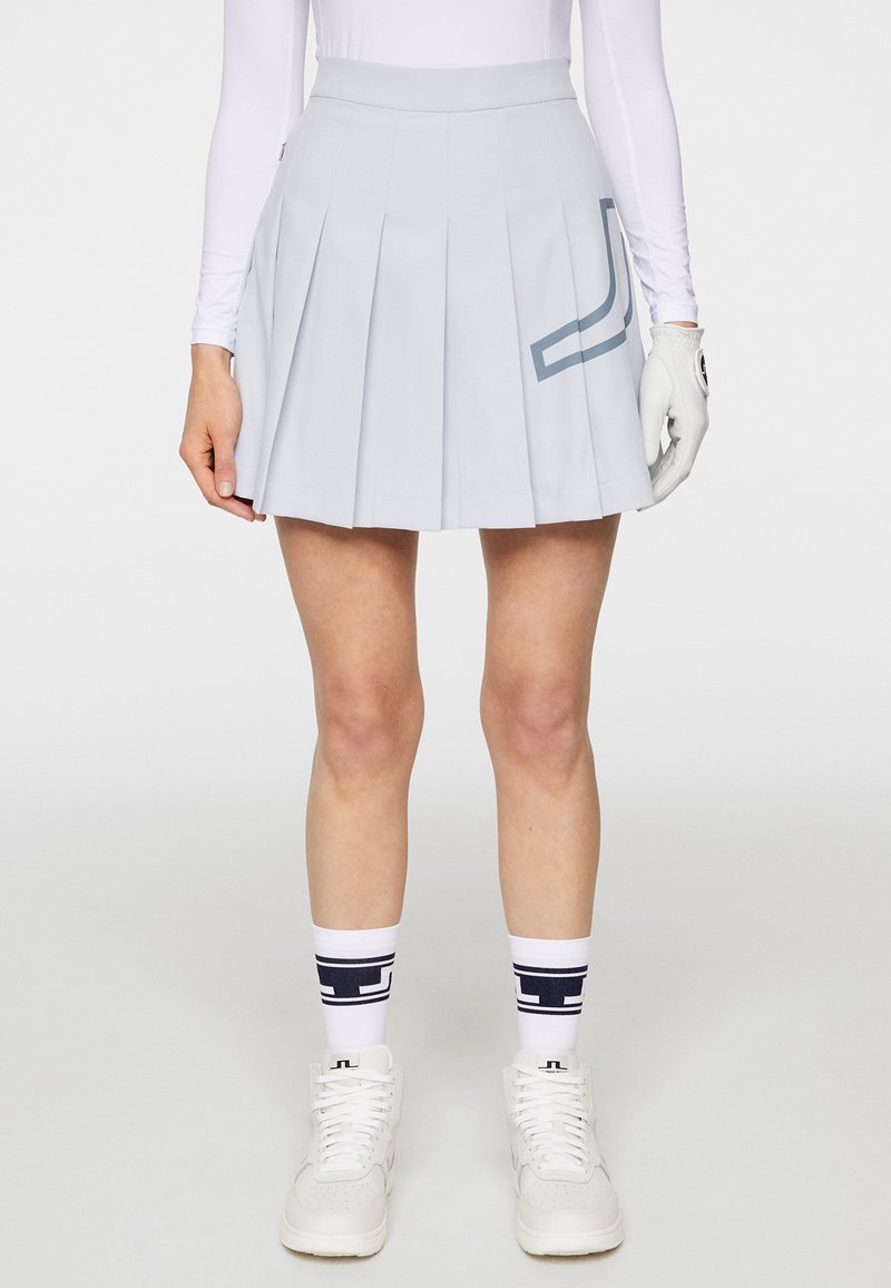 Jasnoniebieska plisowana spódnica z gładką talią oraz akcentem w geometryczny wzór. Noszona z białymi trampkami i granatowymi skarpetkami w wzory.