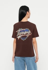 Brown cotton t-shirt featuring a large blue heart graphic with "Tommy" in white and red cursive, outlined in gray, on the back.